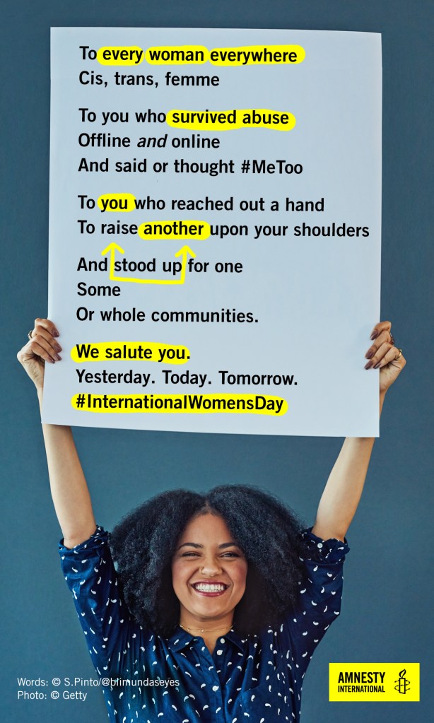 International Women's Day 2018, image of a woman of colour grinning and holding up a poster with the words of a solidarity poem by S. Pinto.